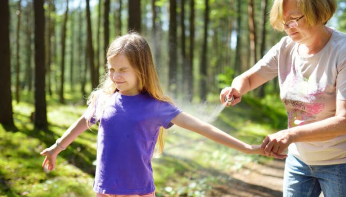 Woman spraying daughter in woods for ticks